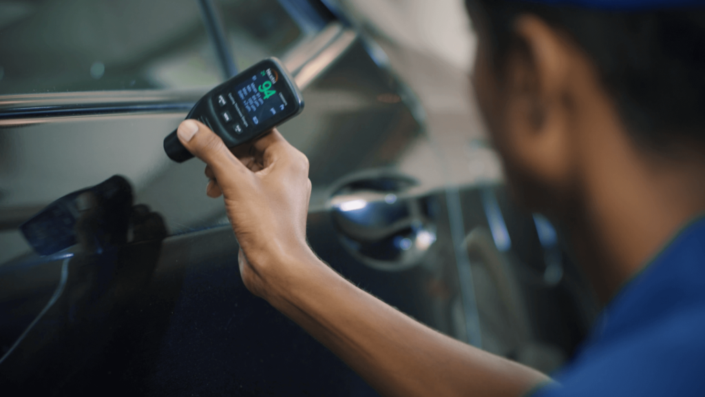 A CarPro team member checking the thickness of the paint on a black car using a elcometer during a car inspection.